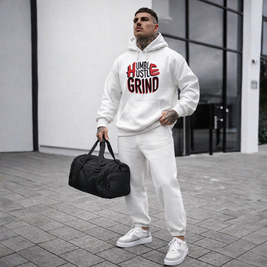 Man in white hoodie and pants holding a black duffel bag with 'Humble Hustle Grind' text.